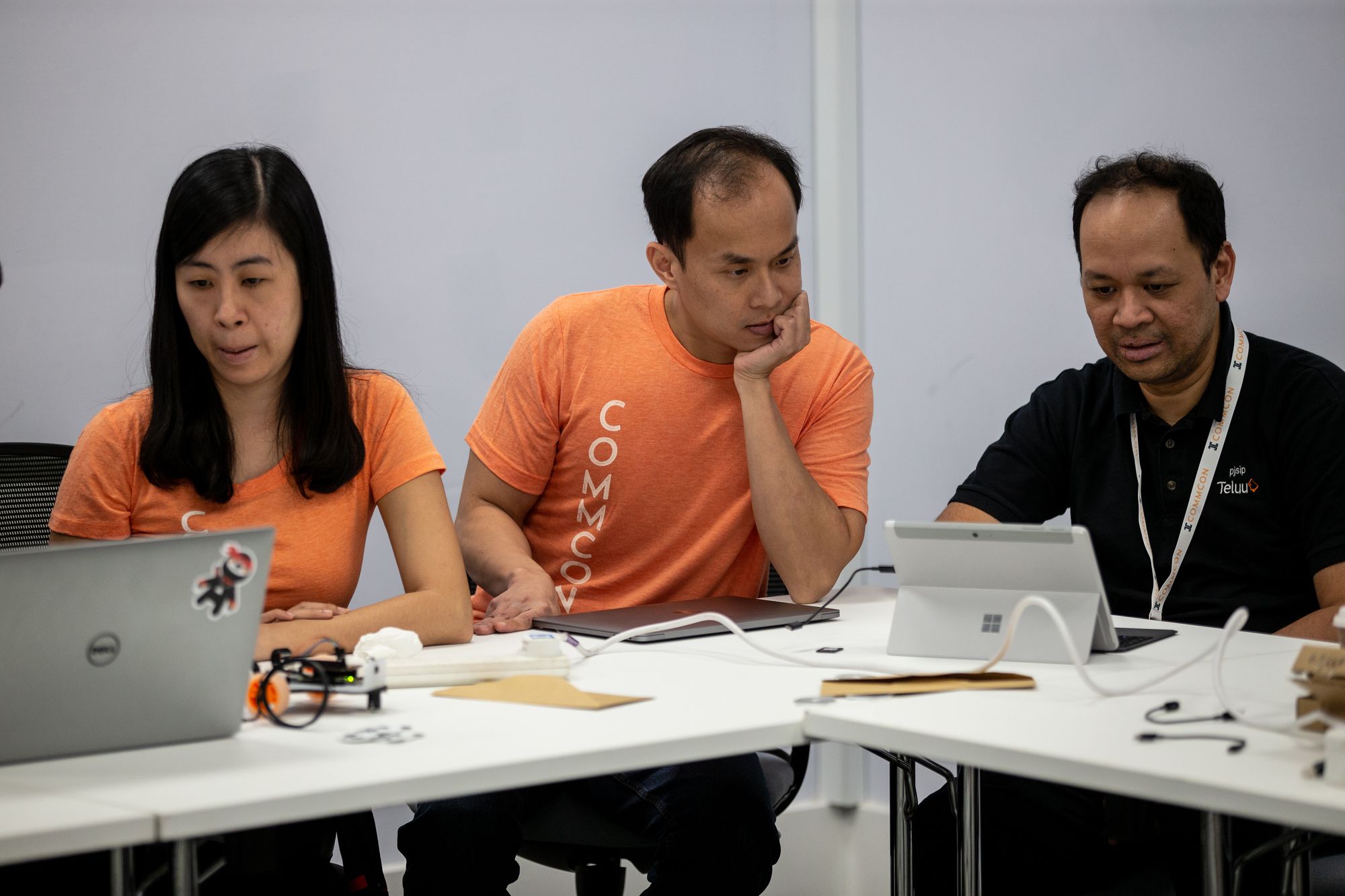 Three people sit at laptops and tablets with some electrical equipment, working together to build a toy car with a working video connection